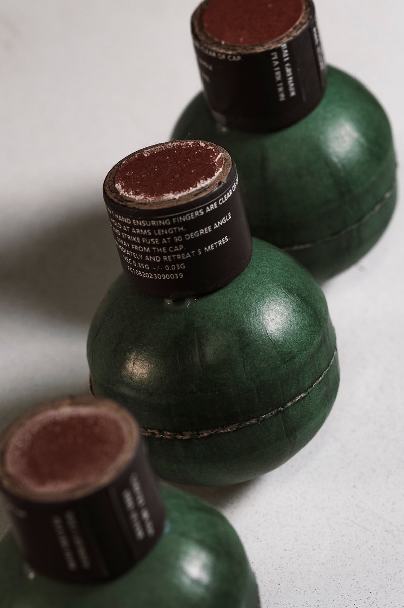 Close-up of green ball grenades with their fuse caps on a white surface