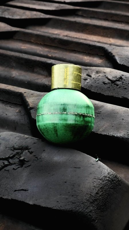 A green ball grenade with a gold cap resting on dark roof tiles