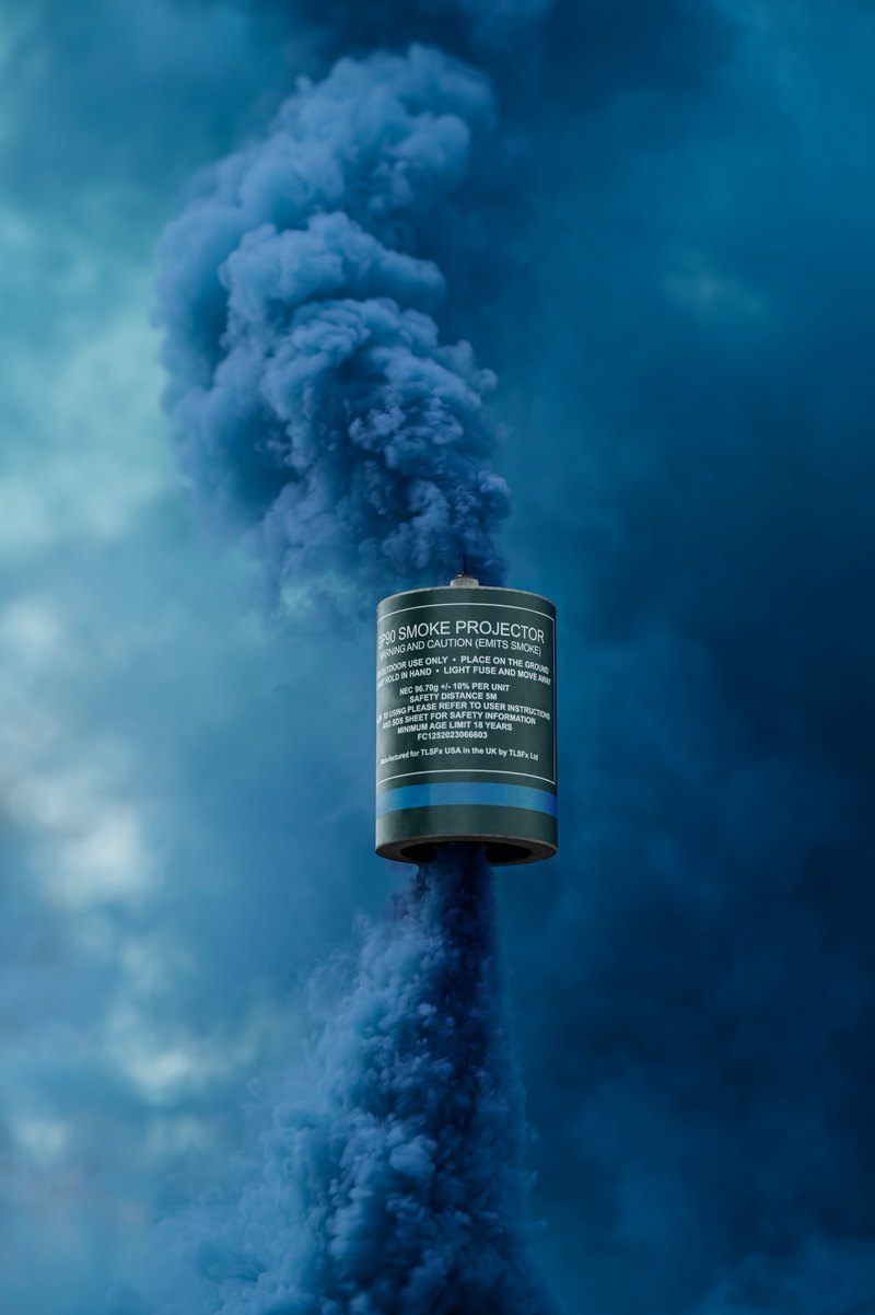 Blue smoke rising from a smoke grenade canister held up on a stake