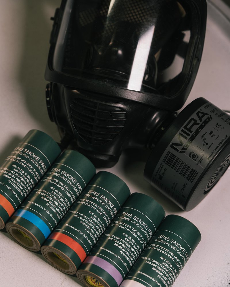 Smoke grenade canisters with coloured bands lying beside a gas mask