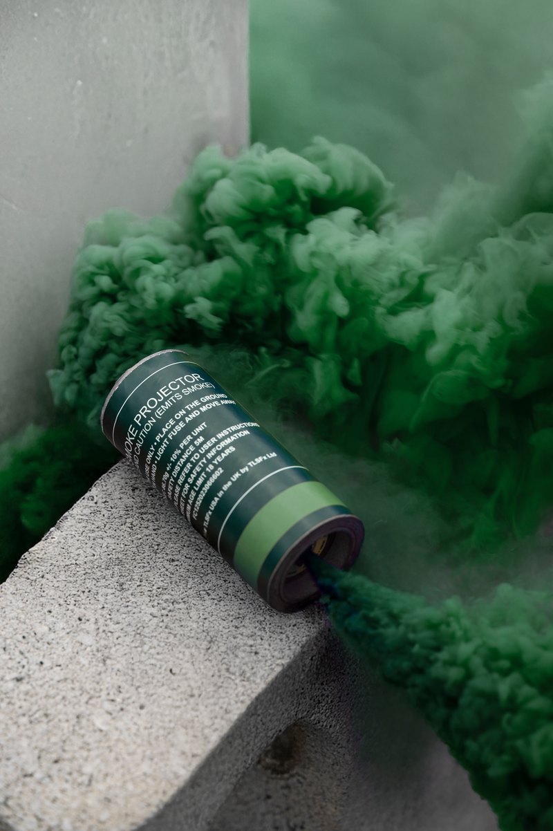 Green smoke pouring from a smoke grenade canister resting on a concrete block