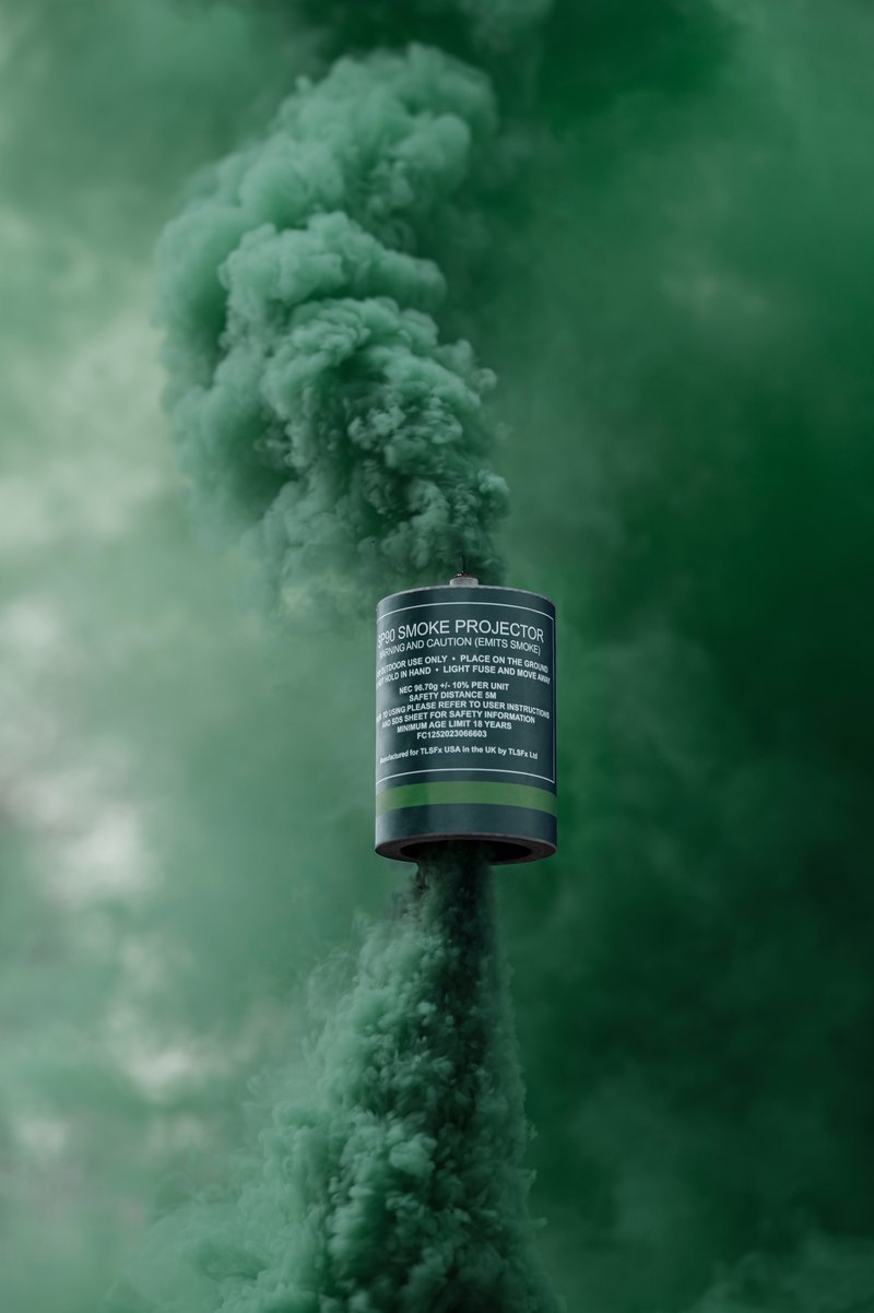 Green smoke rising from a smoke grenade canister held up on a stake