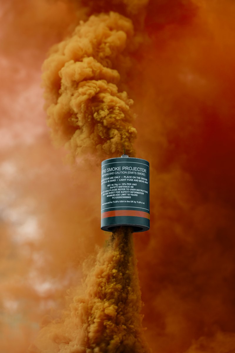 Orange smoke rising from a smoke grenade canister held up on a stake