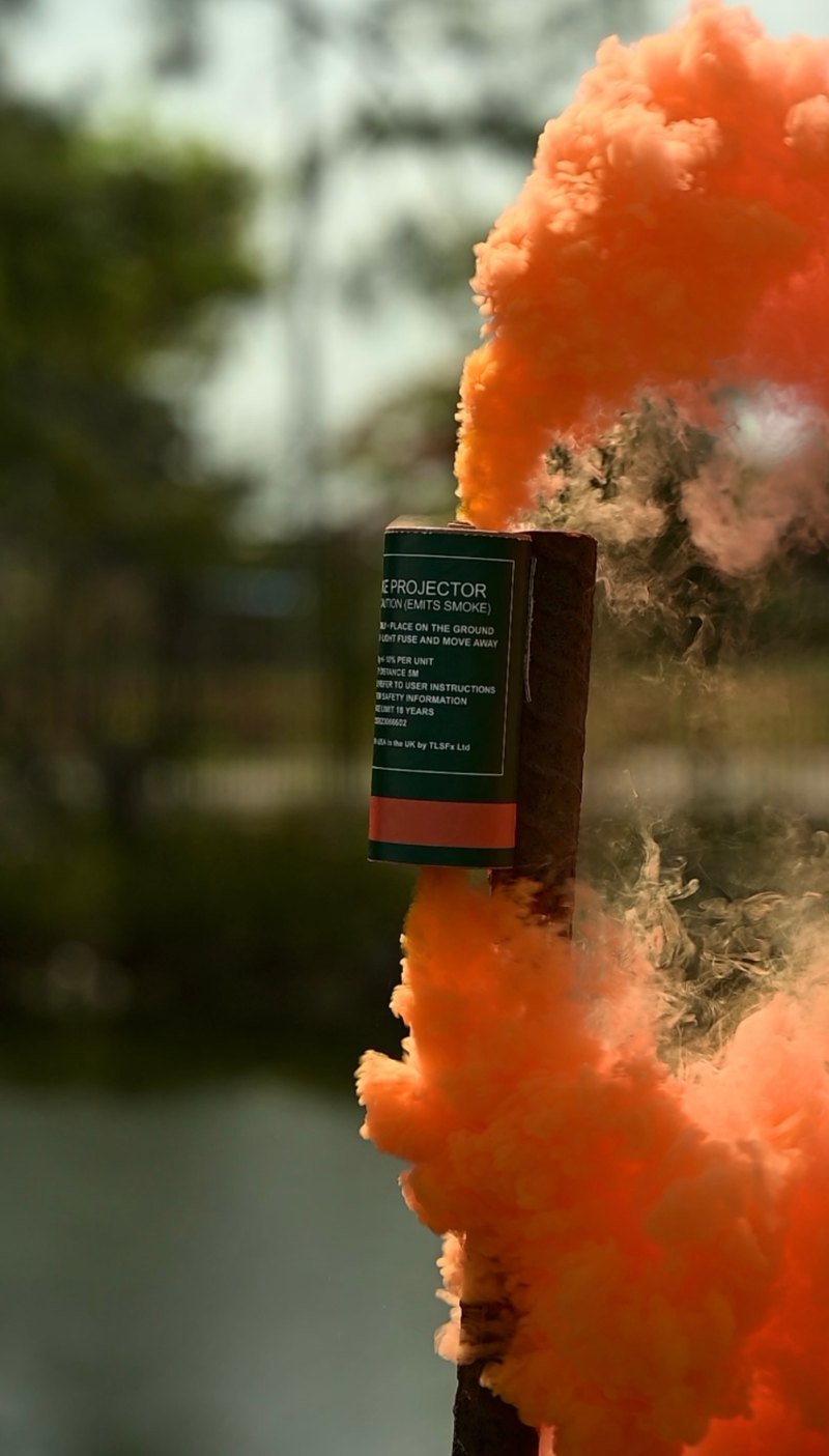Orange smoke rising around a smoke grenade canister against a wooded background