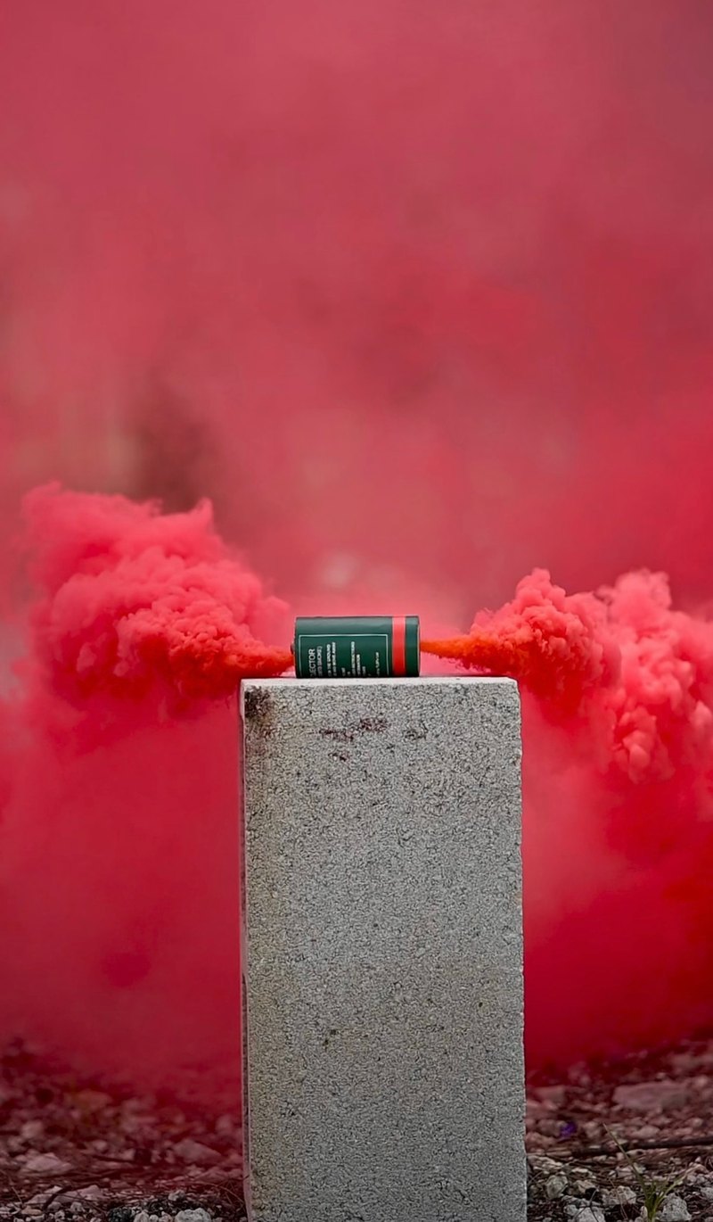 Red smoke streaming sideways from a canister set on a concrete block