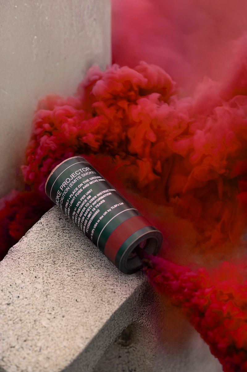 Red smoke pouring from a smoke grenade canister resting on a concrete block