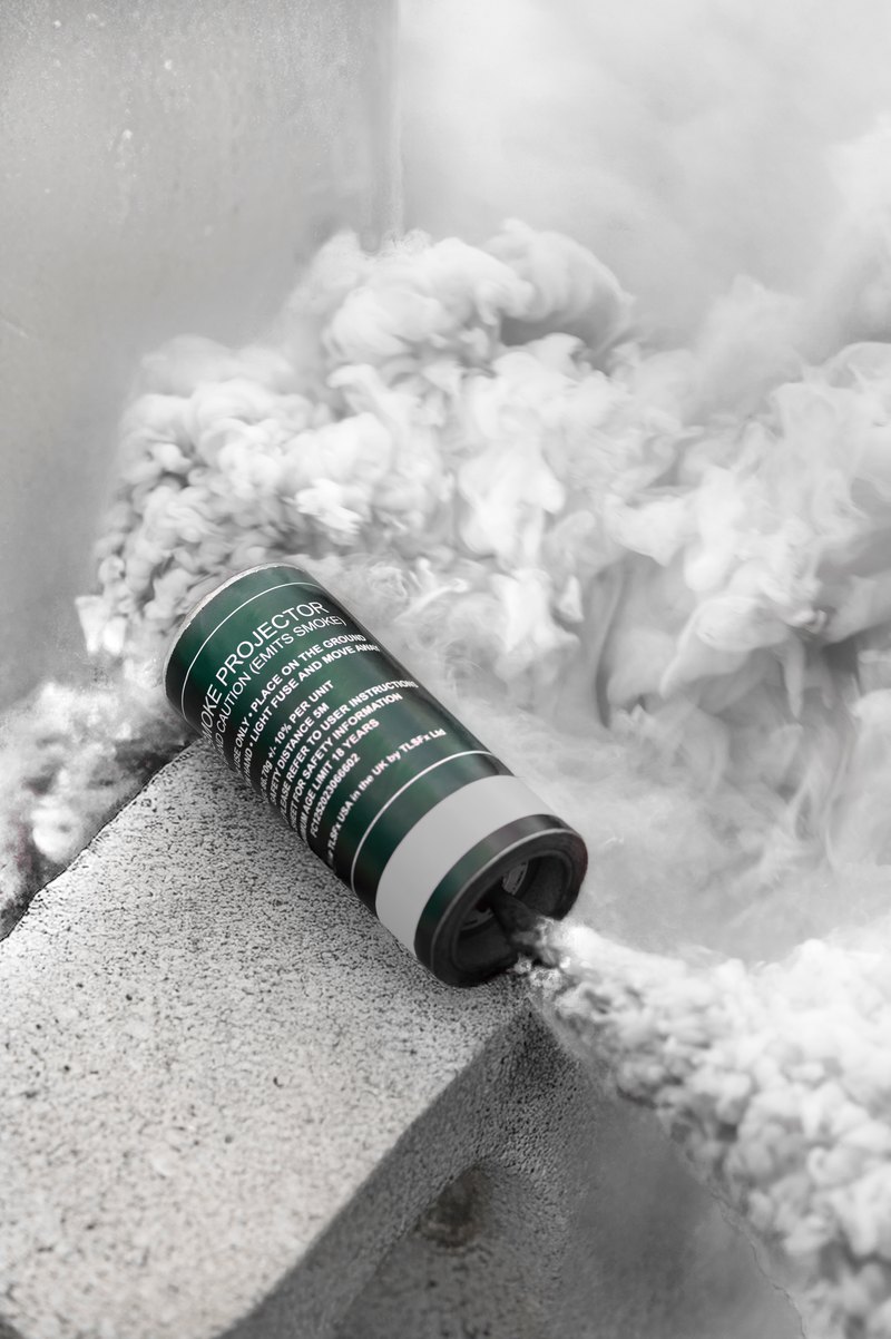 White smoke pouring from a smoke grenade canister resting on a concrete block